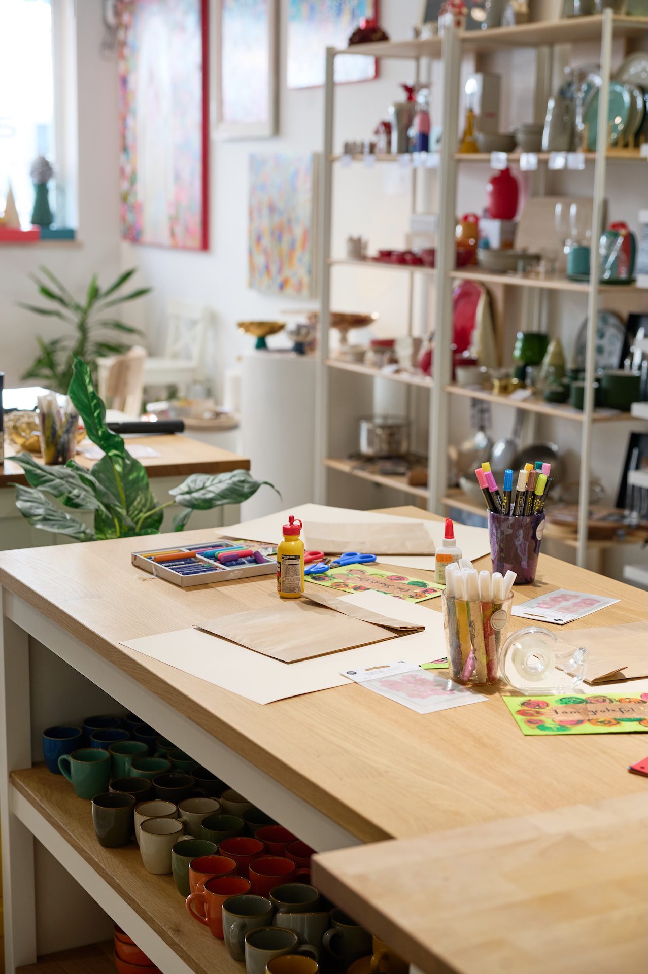Art therapy workspace in Lisbon with a wooden table set up for a creative workshop, featuring markers, paper, glue, and colorful materials, surrounded by plants and handmade ceramics in a bright, calming studio environment.